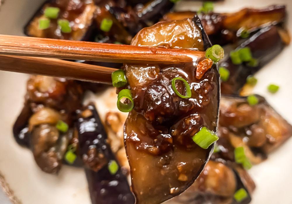 plato blanco sobre un mantel blanco con berenjenas glaseadas con miso y cebollino